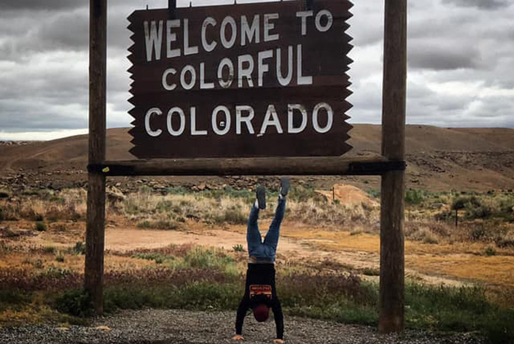 osse doing a handstand in front of a 'Welcome to Colorful Colorado' sign